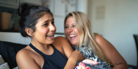 An adult and young person are sitting close together on a sofa. They are both laughing 