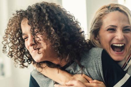 An adult is wrapping a young person in a good-natured hug from behind. They are both laughing 